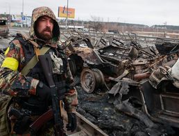 Ein Kämpfer eines ukrainischen Freiwilligenverbandes steht bei der Stadt Bucha vor ausgebrannten russischen Militärfahrzeugen. Foto: picture alliance / Associated Press / Serhii Nuzhnenko