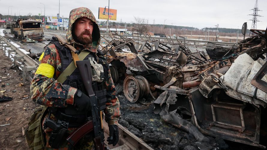 Ein Kämpfer eines ukrainischen Freiwilligenverbandes steht bei der Stadt Bucha vor ausgebrannten russischen Militärfahrzeugen. Foto: picture alliance / Associated Press / Serhii Nuzhnenko