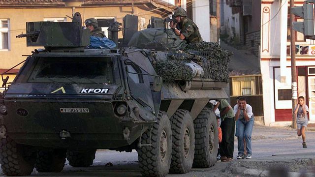 Einsatz im Kosovo: Zivilisten suchen am 13. Juni 1999 in Prizren Deckung hinter einem Transportpanzer der Bundeswehr. Bei dem Schusswechsel kommen zwei bewaffnete serbische Angreifer ums Leben. Foto: picture-alliance/dpa/AFP Christophe Simon