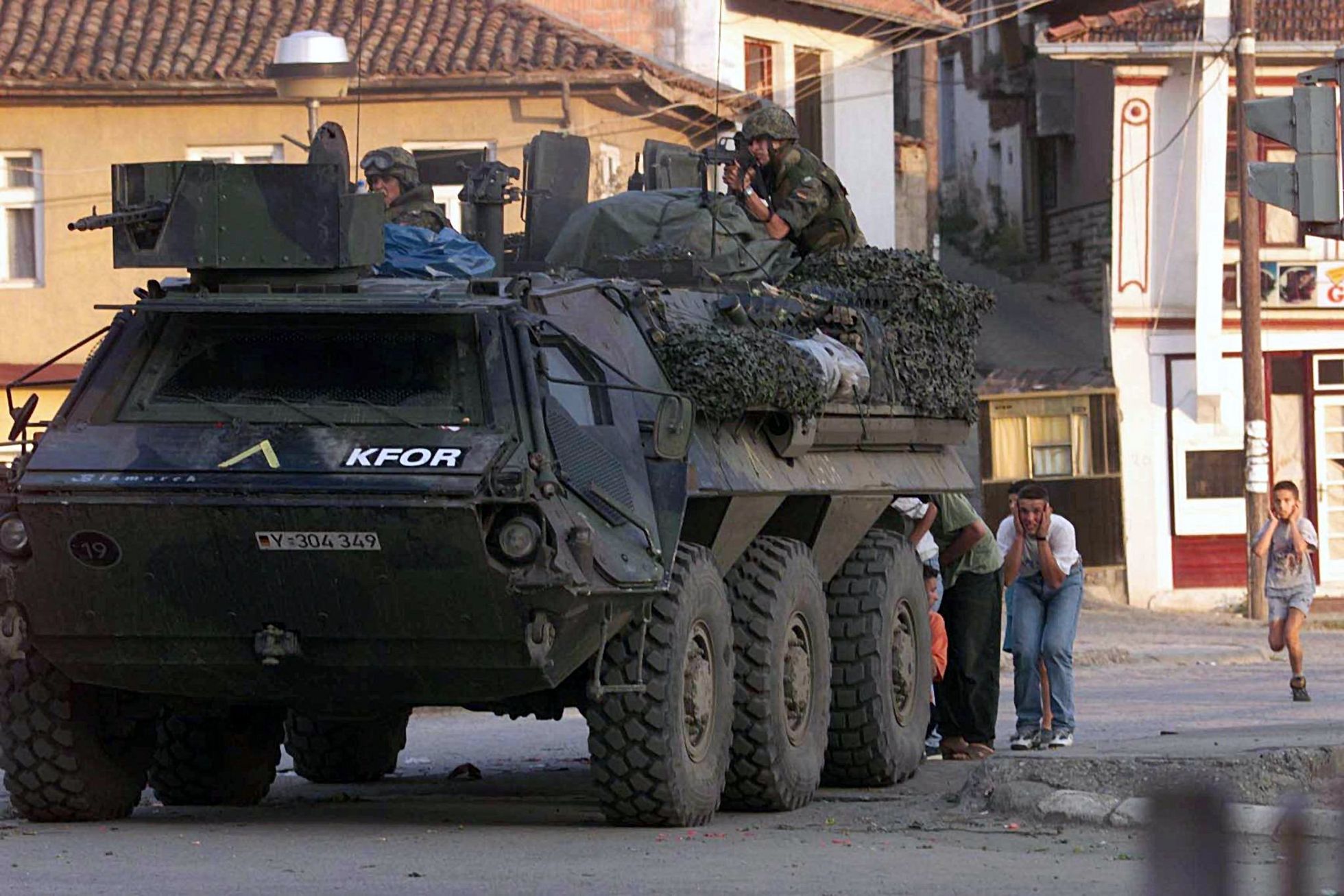 Zivilisten suchen am 13. Juni 1999 in Prizren Deckung hinter einem Transportpanzer der Bundeswehr. Bei dem Schusswechsel kommen zwei bewaffnete serbische Angreifer ums Leben. 