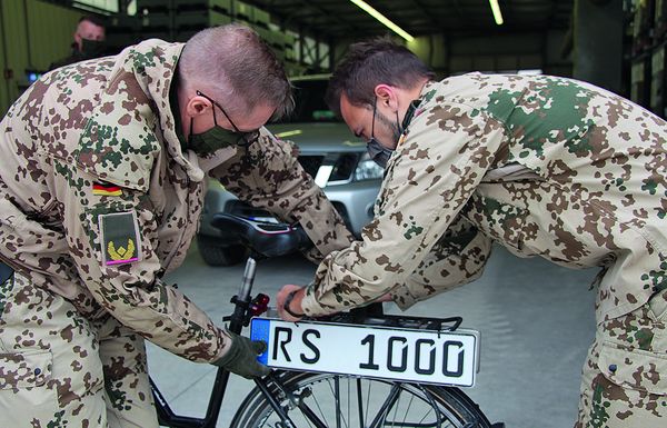 Zwei Soldaten des deutschen Einsatzkontingents Resolute Support befestigen ein Kfz-Zeichen an einem Fahrrad. Foto: Bundeswehr/Schachel