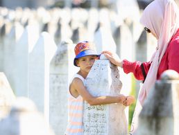 Gedenken zum 29. Jahrestag des Massakers von Srebrenica: Ein bosnischer Junge mit seiner Mutter an einem Grabstein in der Gedenkstätte in Potocari unweit von Srebrenica. Foto: picture alliance/REUTERS/Amel Emric